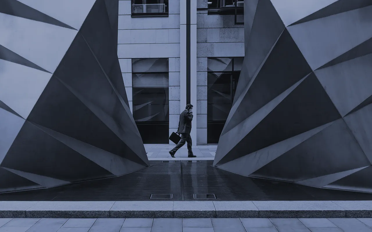 A single figure with a briefcase crossing a plaza between two faceted steel forms.